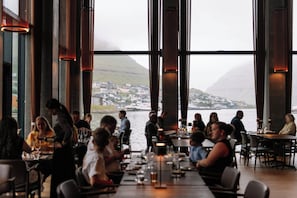Un restaurant doté de grandes fenêtres donnant sur un plan d’eau et sur une ville située au loin.