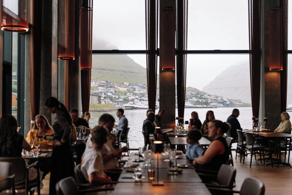 Restaurante con amplios ventanales que dan a una masa de agua y un pueblo lejano.