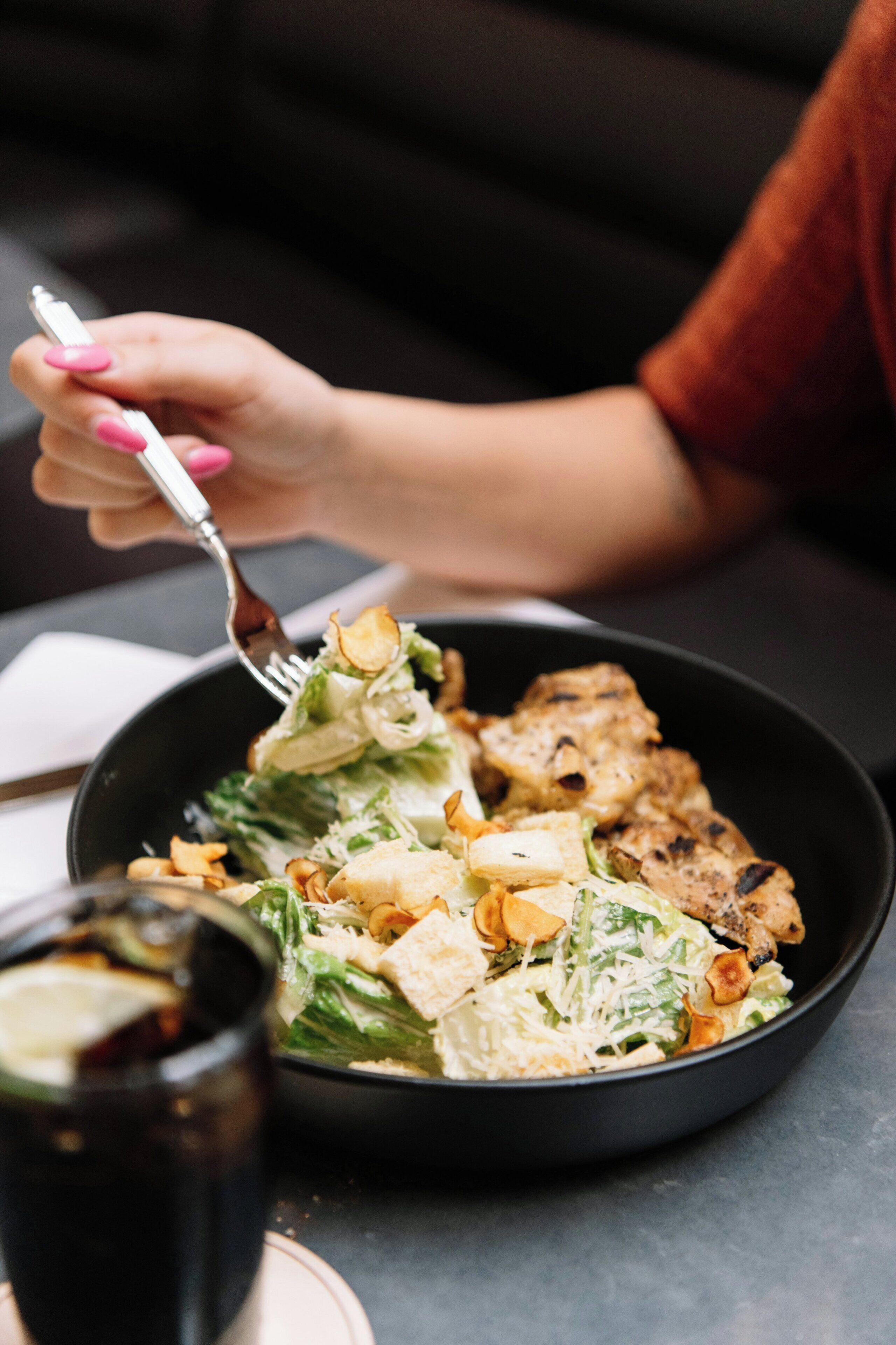 Una persona sosteniendo un tenedor con un bol de ensalada que contiene lechuga, crutones y pollo a la parrilla.