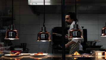A kitchen with hanging pendant lights, a chef preparing food, and plates of food on the counter.