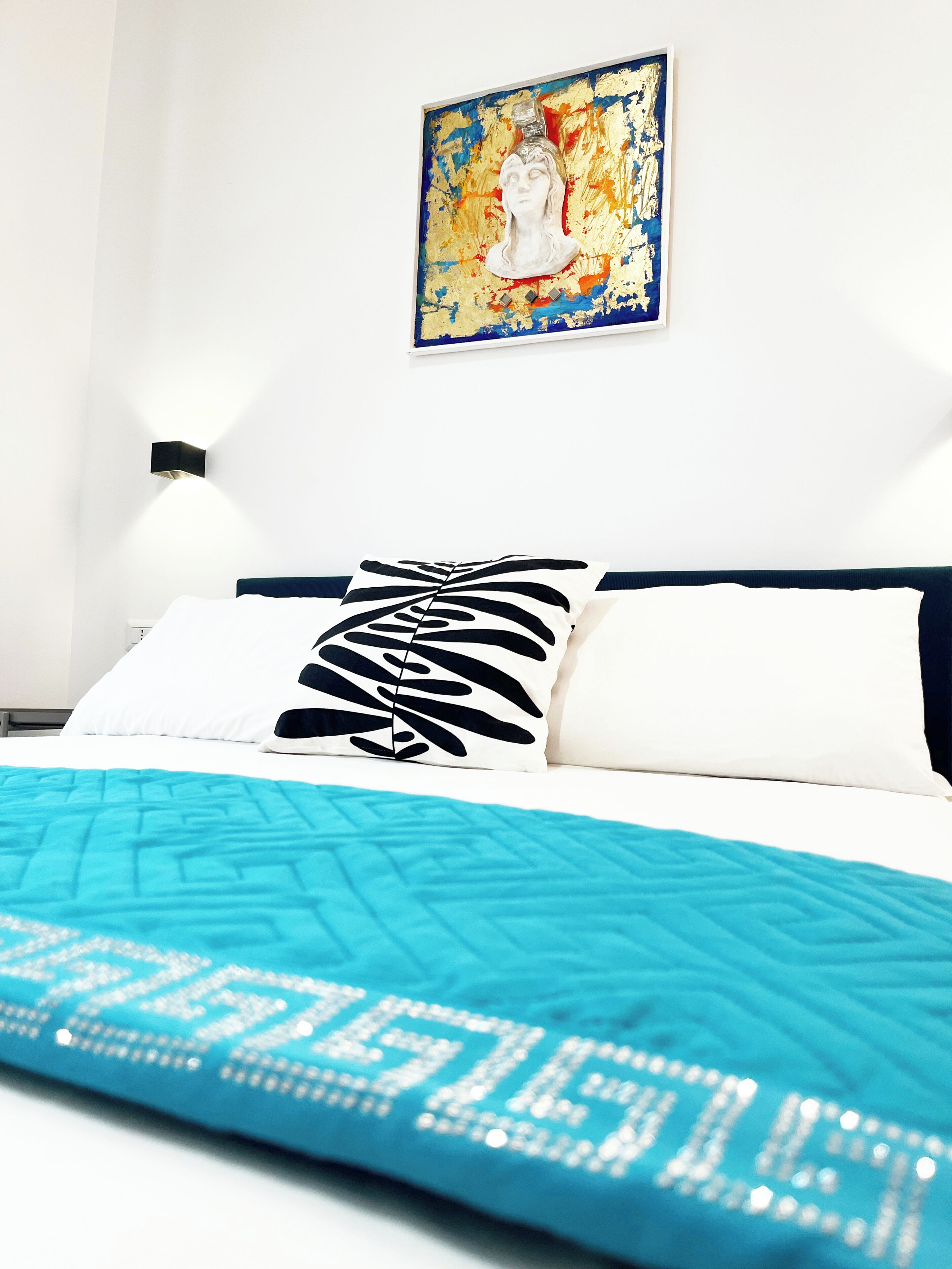 A bed with a blue quilt, white pillows, and a black and white patterned pillow.