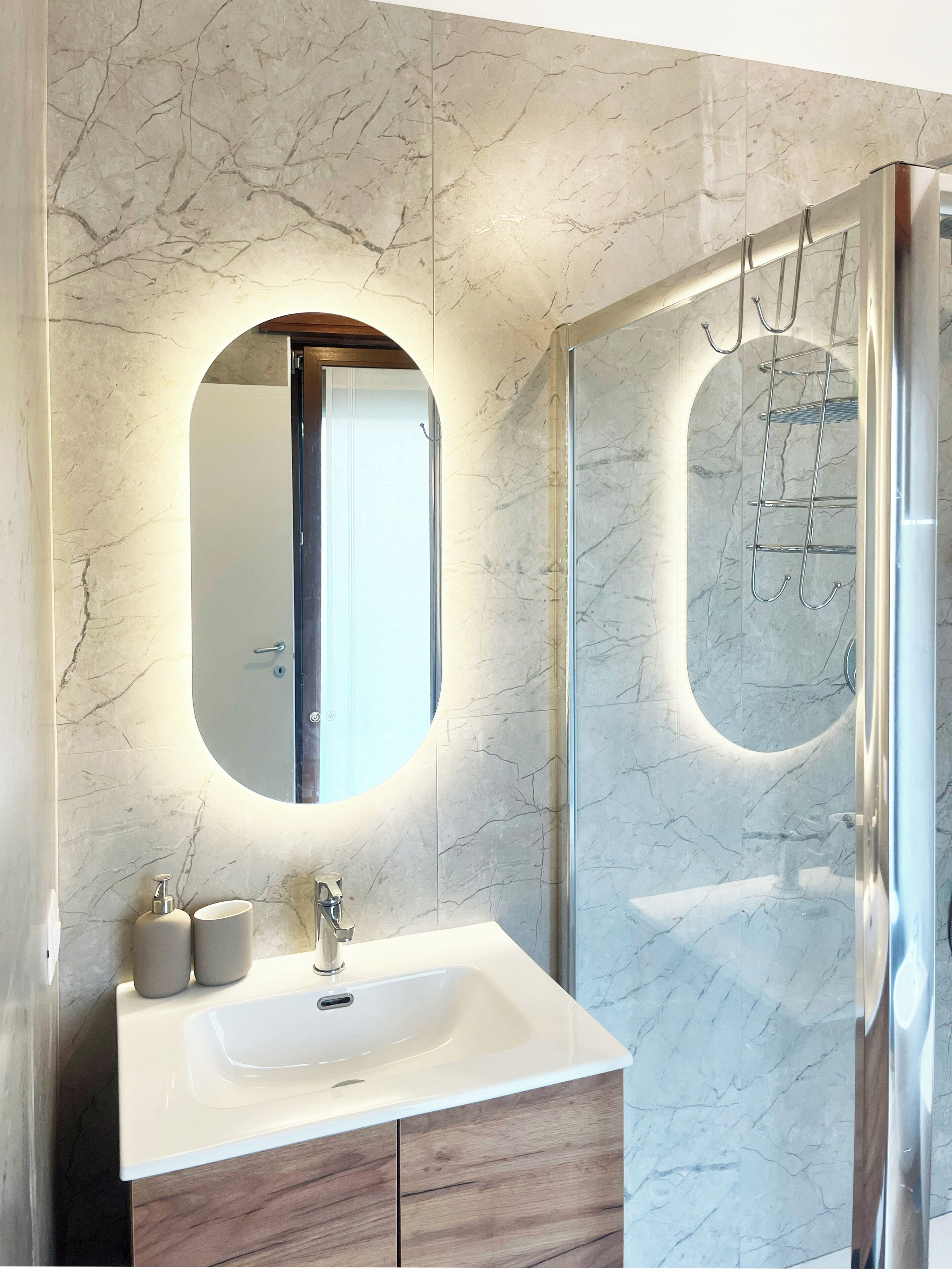 Un bagno moderno con parete in marmo, uno specchio rotondo, un lavandino con rubinetto e una cabina doccia in vetro.