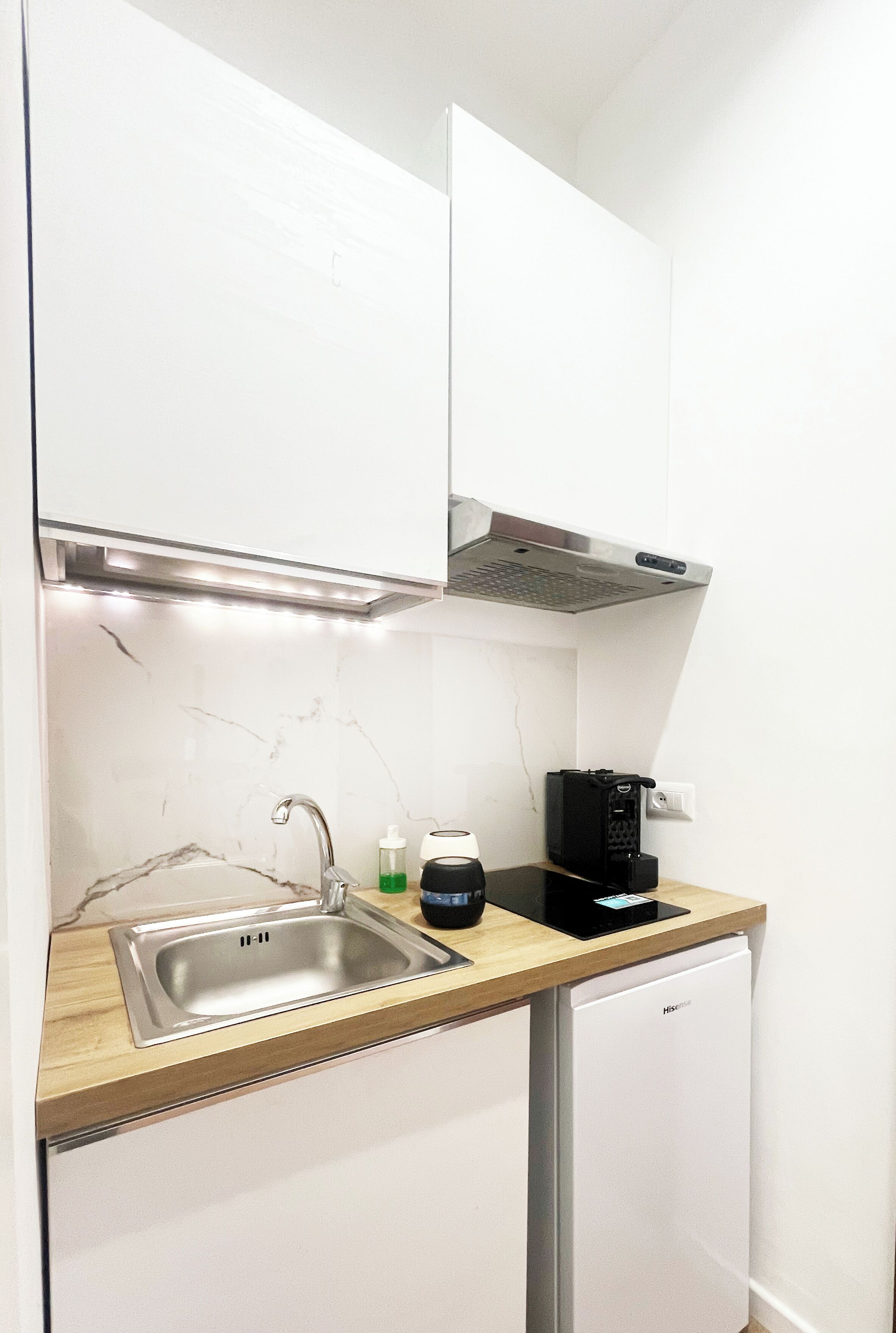 Een compacte keuken met een roestvrijstalen spoelbak, een koffieapparaat en een kleine koelkast.