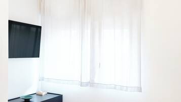Un dormitorio con una cama, una mesita de noche negra, un televisor y una araña.