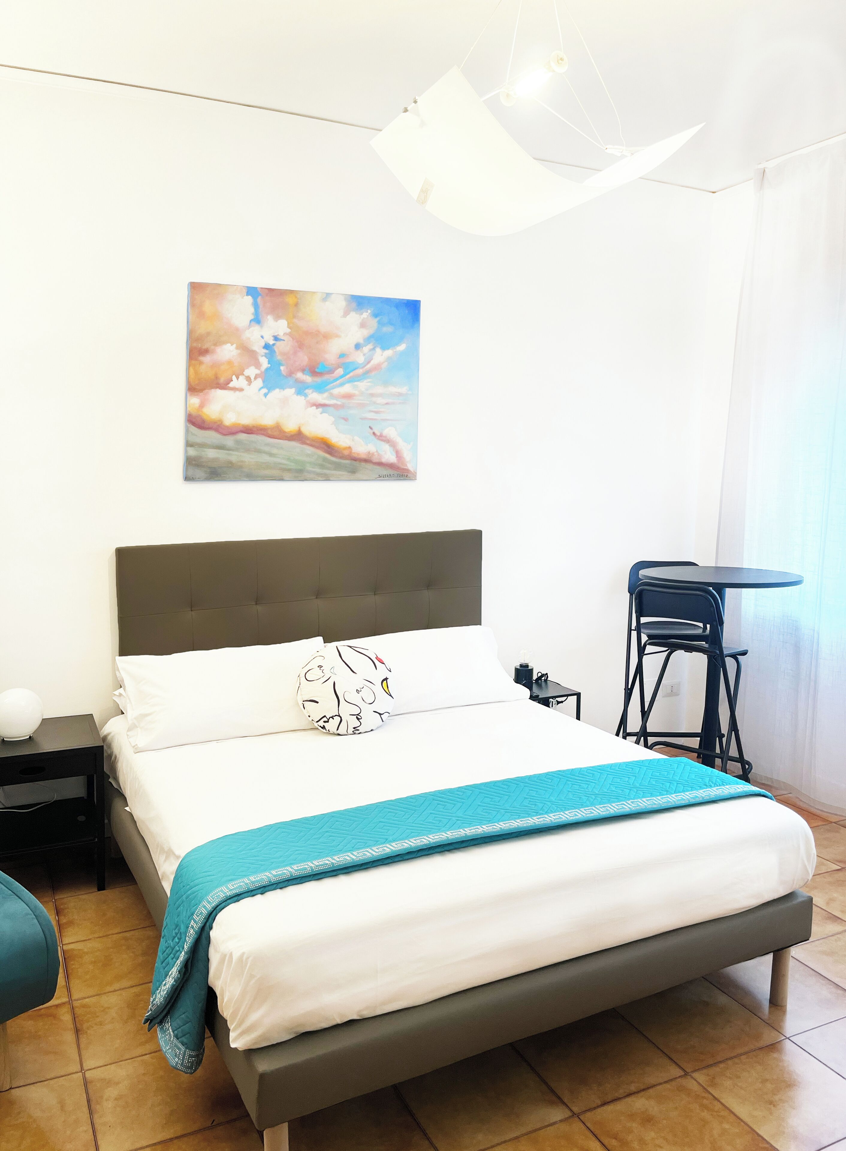 Una habitación de hotel con una cama, una mesita de noche, una silla, una pequeña mesa y un cuadro en la pared.