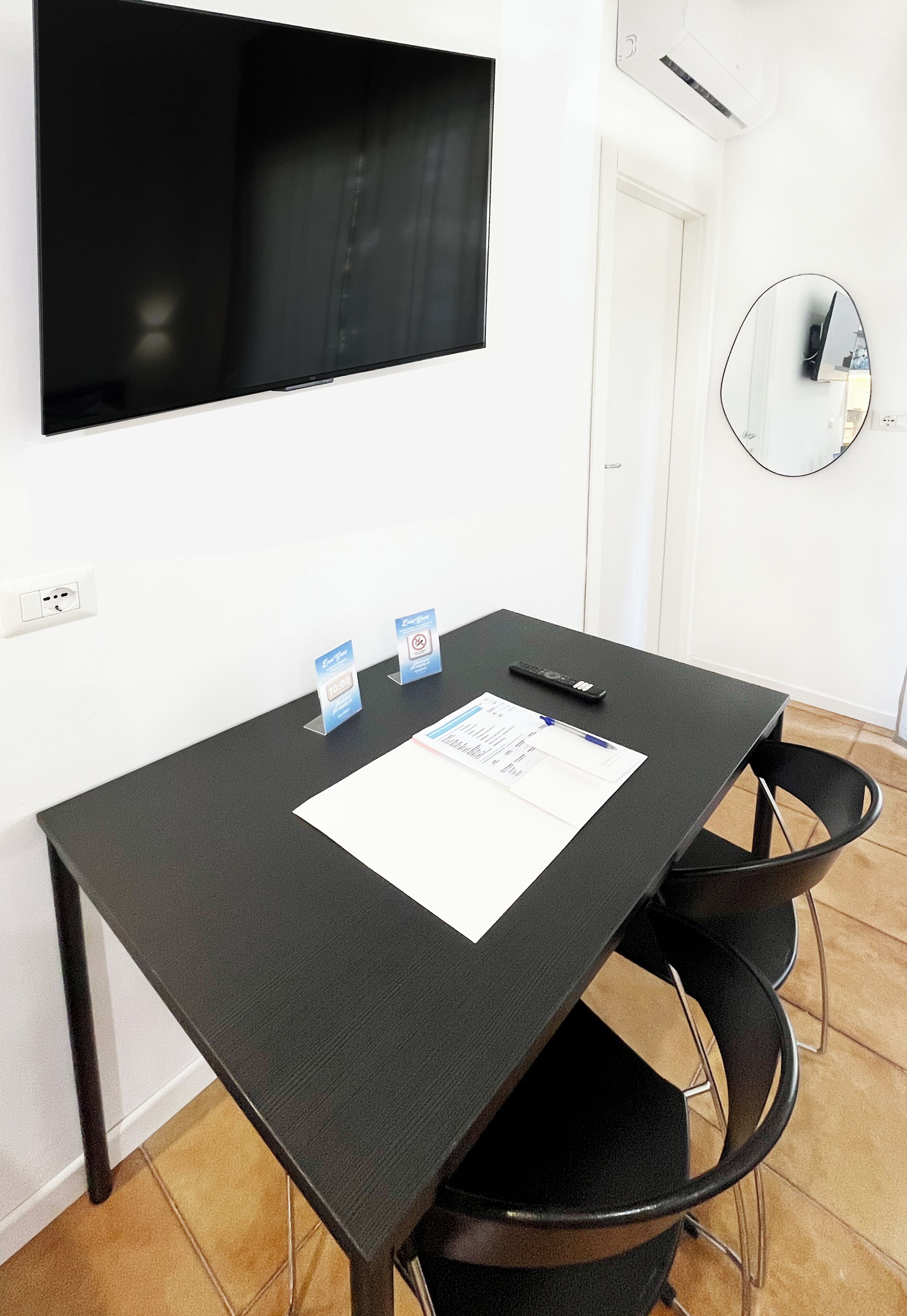 A conference table with chairs, a flat-screen TV mounted on the wall, a round mirror, and a door.