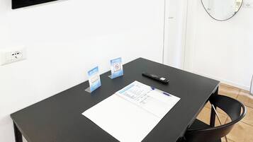 A conference table with chairs, a flat-screen TV mounted on the wall, a round mirror, and a door.