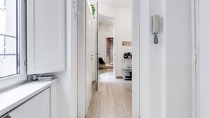 Un couloir avec une porte blanche, un téléphone et une étagère sur laquelle sont posés divers objets.