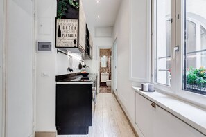 Eine schmale Küche mit einem schwarzen Kühlschrank, weißen Schränken und einem Fenster mit Blick nach draußen.