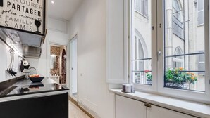 Une cuisine moderne avec un plan de travail noir, un saladier rempli de fruits et une fenêtre donnant sur des bâtiments et des fleurs.