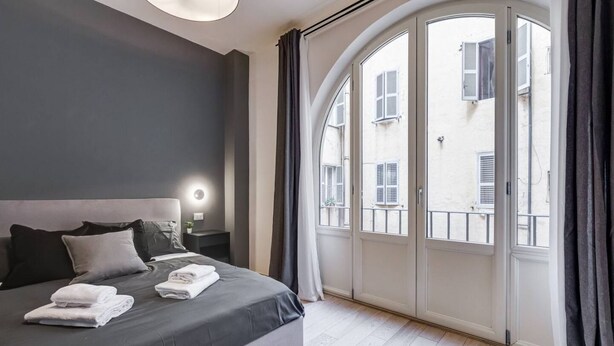 Une chambre moderne avec un grand lit, une table de chevet, une commode et une vue dégagée sur l’extérieur grâce à une grande fenêtre en arc de cercle.