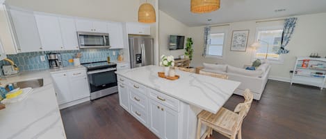 A modern kitchen with white cabinets, stainless steel appliances, and a large island with a wooden chair.