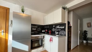 A compact kitchen with a refrigerator, oven, and a black backsplash with food-themed graphics.