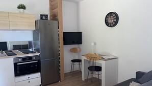Une cuisine moderne dotée d’un réfrigérateur et d’une cuisinière encastrés, un coin repas avec une petite table et des chaises, et un espace de vie avec un canapé.