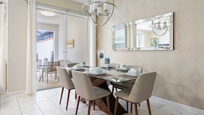 A dining area with a glass-top table, four chairs, a chandelier, and a large mirror on the wall. - Storey Lake 4BR Home - Private Pool (Kissimmee)