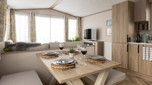 A modern kitchen with wooden cabinets, a dining table set for four, and a TV in the background. - The Beach Hut, Burghead Holiday Park (Burghead)