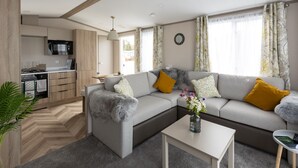 A modern living room with a grey sofa, a white coffee table, and a kitchen area with a microwave and cabinets. - The Beach Hut, Burghead Holiday Park (Burghead)