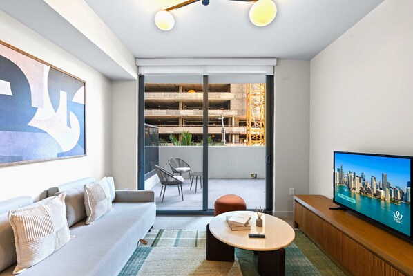 Ein modernes Wohnzimmer mit einer Couch, einem Couchtisch, einem Fernseher und einer Schiebetür zu einem Balkon mit Blick auf ein Baugerüst.