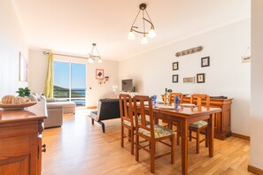 Uma sala de estar ampla com uma mesa de jantar, cadeiras de madeira, um sofá e uma televisão.