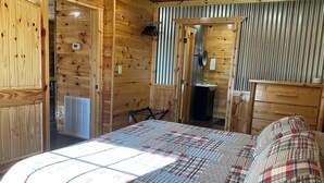 A wooden cabin room with a bed, a small bathroom, and a wooden wardrobe. - Red Cozy Cottage  1-bedroom cottage in charming Oneida, TN (Oneida)