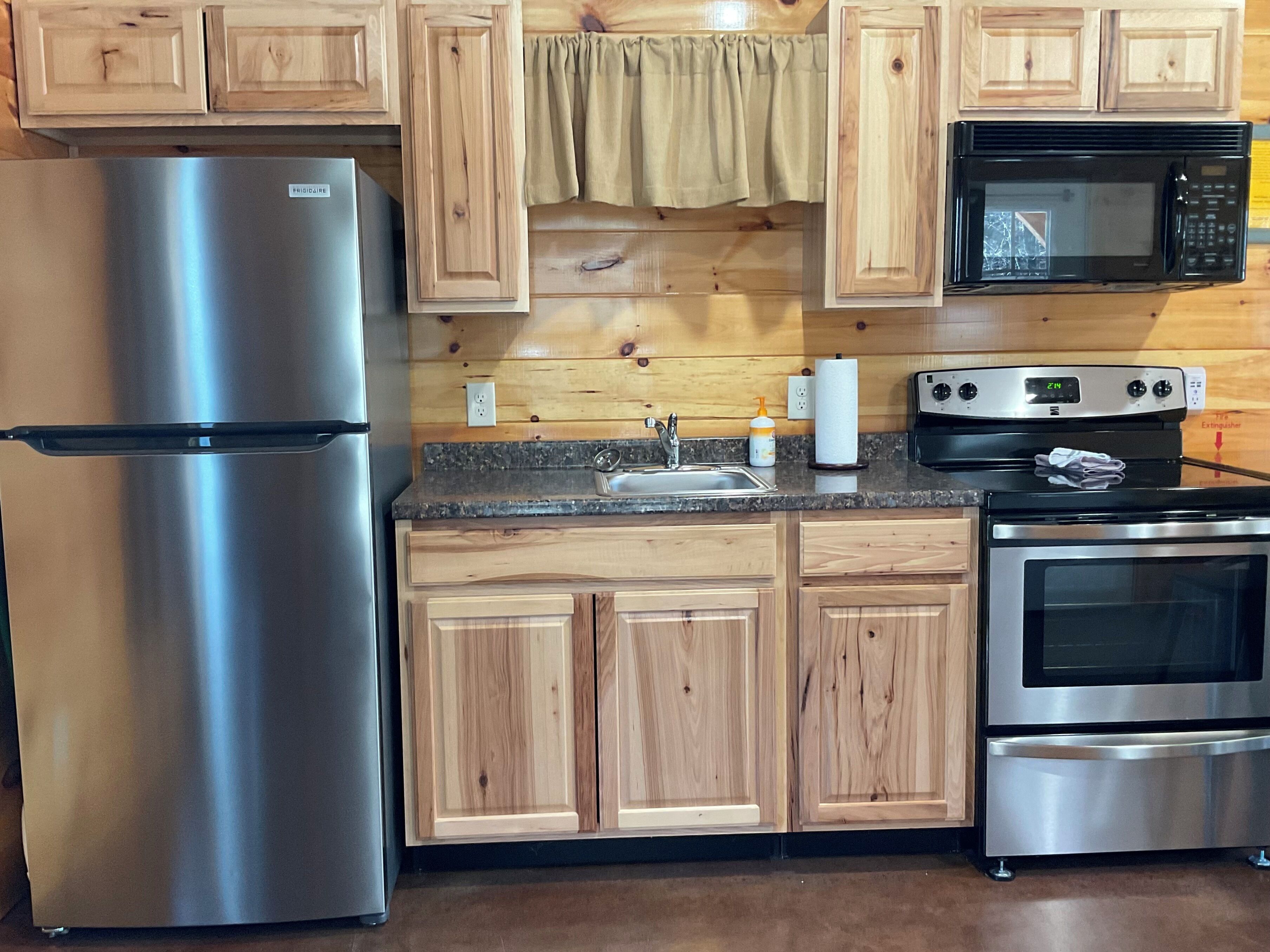 A kitchen with wooden cabinets, a stainless steel refrigerator, a microwave, and an oven.