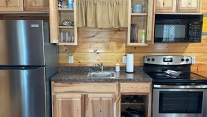 A kitchen with wooden cabinets, a stainless steel refrigerator, a microwave, a stove, and a sink. - Red Cozy Cottage  1-bedroom cottage in charming Oneida, TN (Oneida)