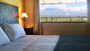 A bedroom with a bed, a nightstand with a lamp, a window with a view of mountains. - Tupungato Divino (Tupungato)