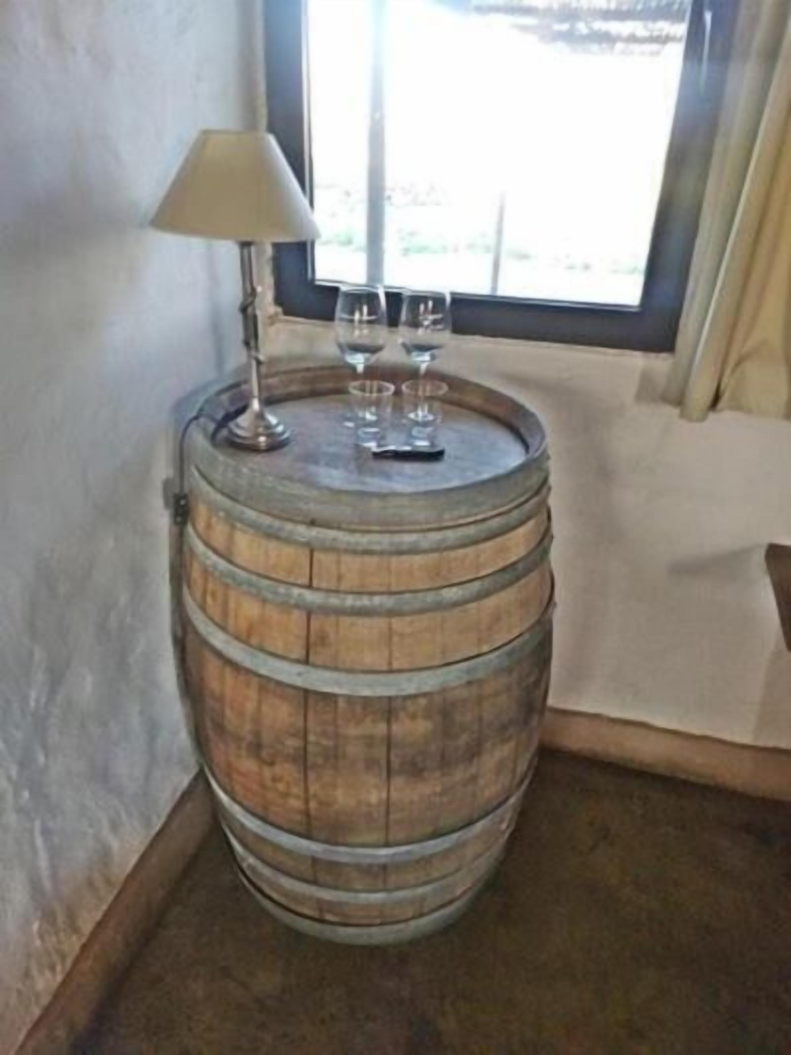 Un barril de madera utilizado como mesa, con una lámpara y dos vasos encima.