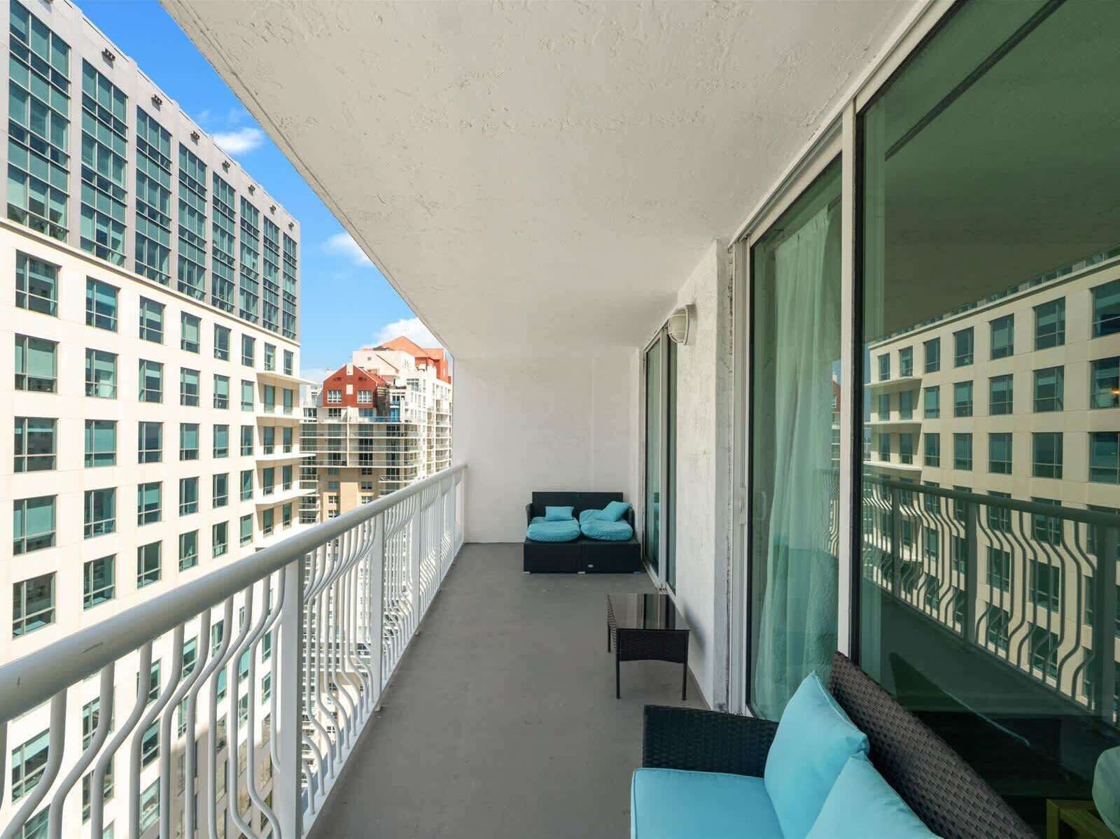 Un balcon donnant sur des immeubles de grande hauteur, un coin salon avec des coussins et une balustrade.
