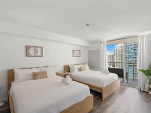 Une chambre d’hôtel avec deux lits, une vue sur la ville et un balcon agrémenté d’une plante.