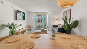 Una sala moderna con una mesa de comedor de madera, una lámpara colgante trenzada y grandes ventanales con vista a un paisaje urbano.