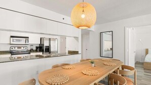 Una cocina moderna con electrodomésticos integrados, un comedor con mesa y sillas de madera, y una lámpara colgante.