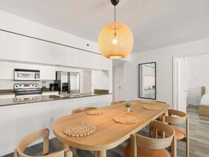 A modern kitchen with built-in appliances, a dining area with a wooden table and chairs, and a hanging light fixture. - Brickell 1BR • Skyline / Pool • FIFA Fan Fest (Miami)