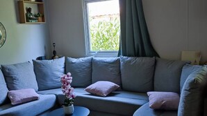 A living room with a grey sofa, a small round table, and a potted orchid. - 6 person mobile home "La Pagode" in a family campsite**** (Fréjus)