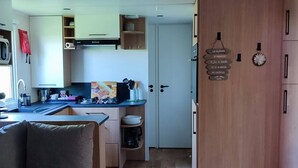 A compact kitchen with a sink, stove, and cabinets. There is a door with a sign indicating directions to the bathroom and garden. - 6 person mobile home "La Pagode" in a family campsite**** (Fréjus)