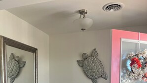 Um corredor com uma porta rosa, um ventilador de teto, um espelho e duas peças de arte com tema de tartarugas.