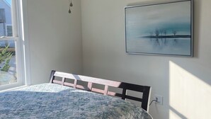 Quarto com cama, ventoinha no teto, janela e um quadro na parede.