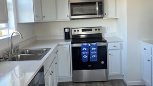Una cocina con armarios blancos, un microondas de acero inoxidable, una estufa y un lavavajillas.