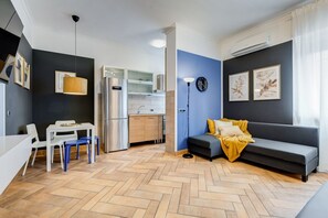 Ein gemütlicher Wohnraum mit Küchenzeile, Essbereich, einer Couch und einer Stehlampe.