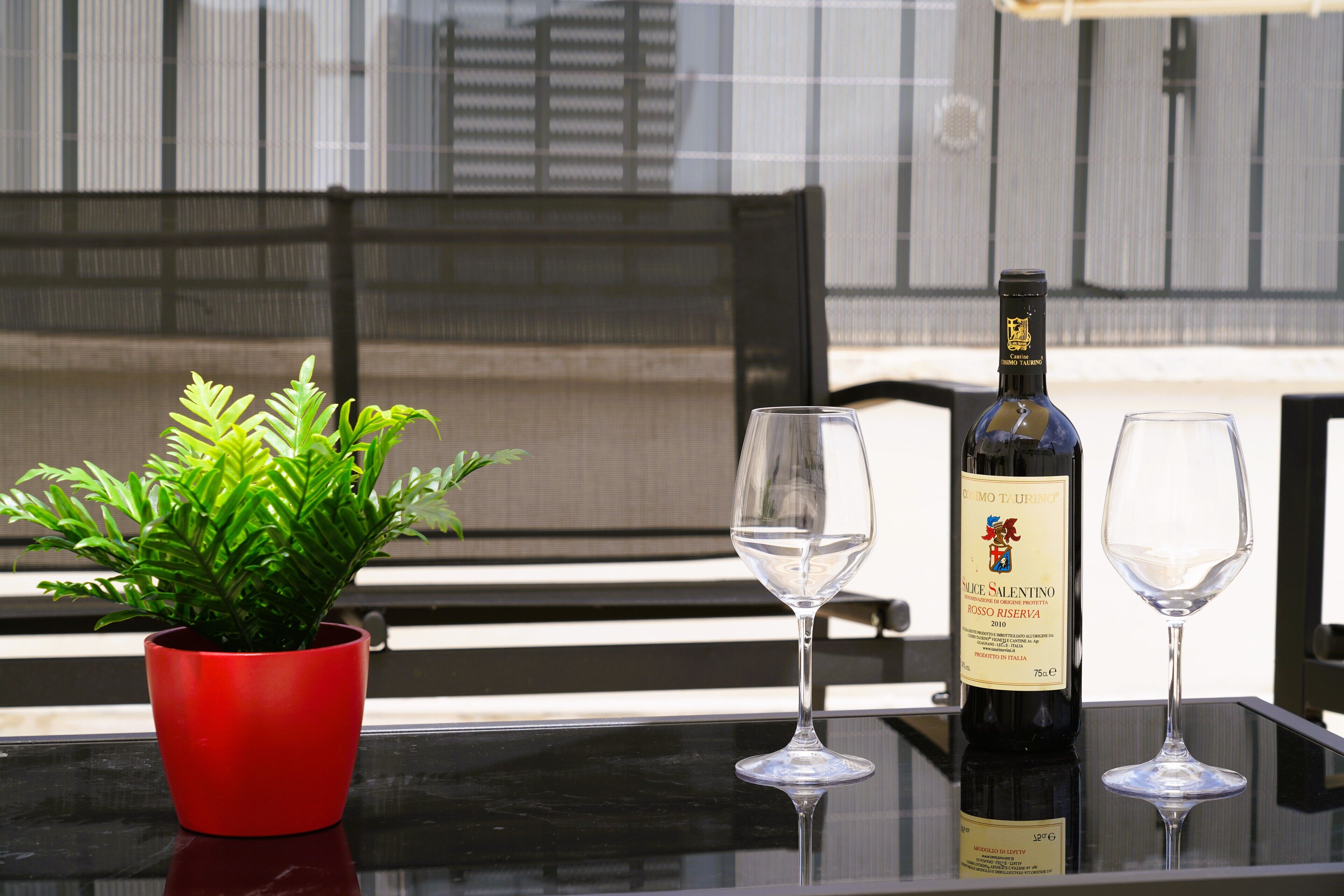 Une table avec une bouteille de vin, deux verres et une plante en pot aux feuilles rouges.