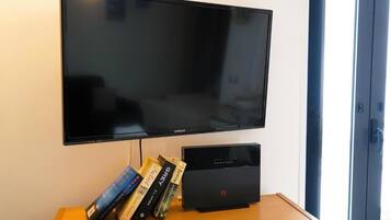 Ein flachbildfernseher an der Wand, ein Holztisch mit Büchern und einem schwarzen elektronischen Gerät, und eine Tür zur rechten Seite.