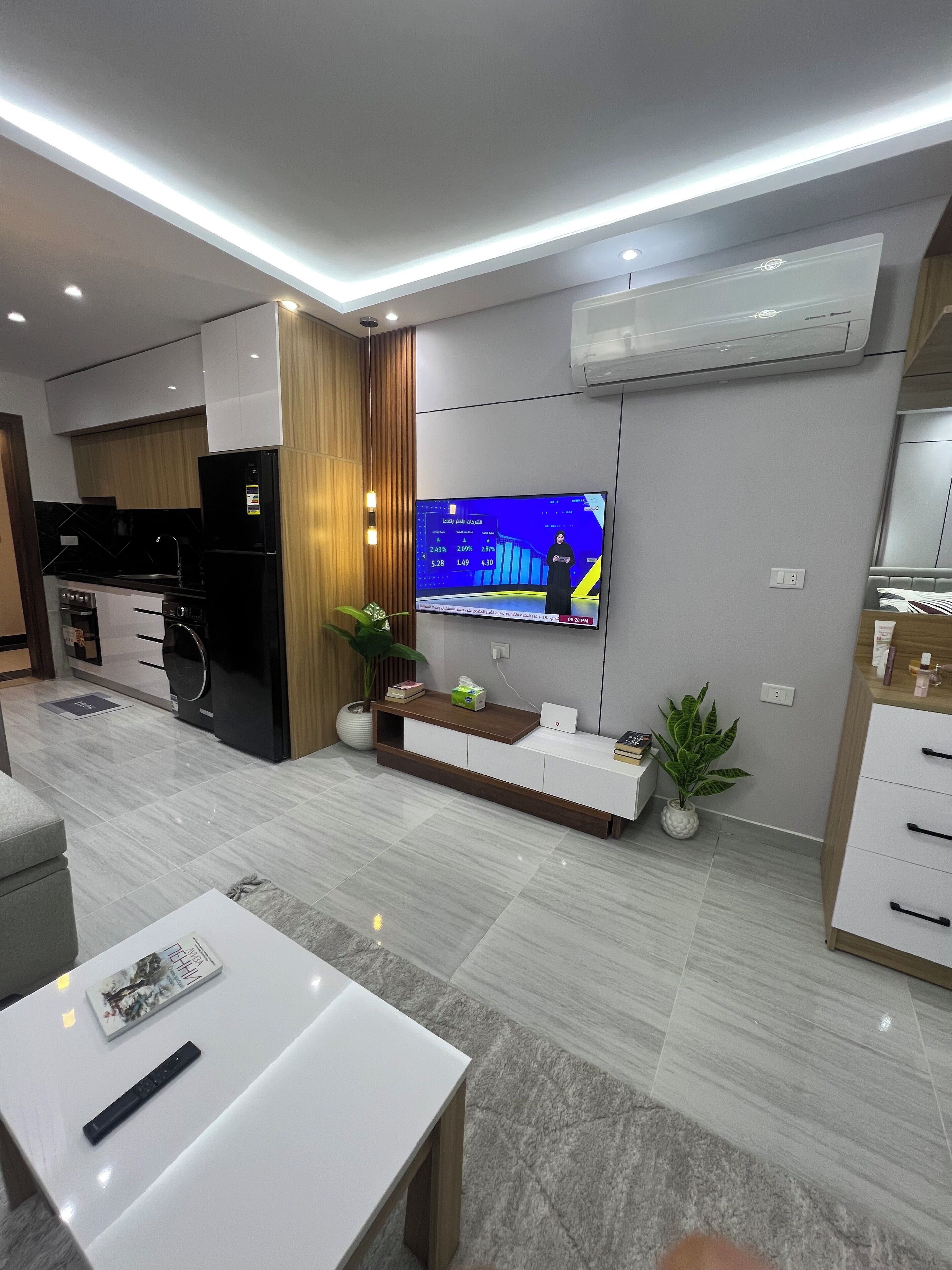 A modern living room with a flat-screen TV, a kitchen area, and a dining space.