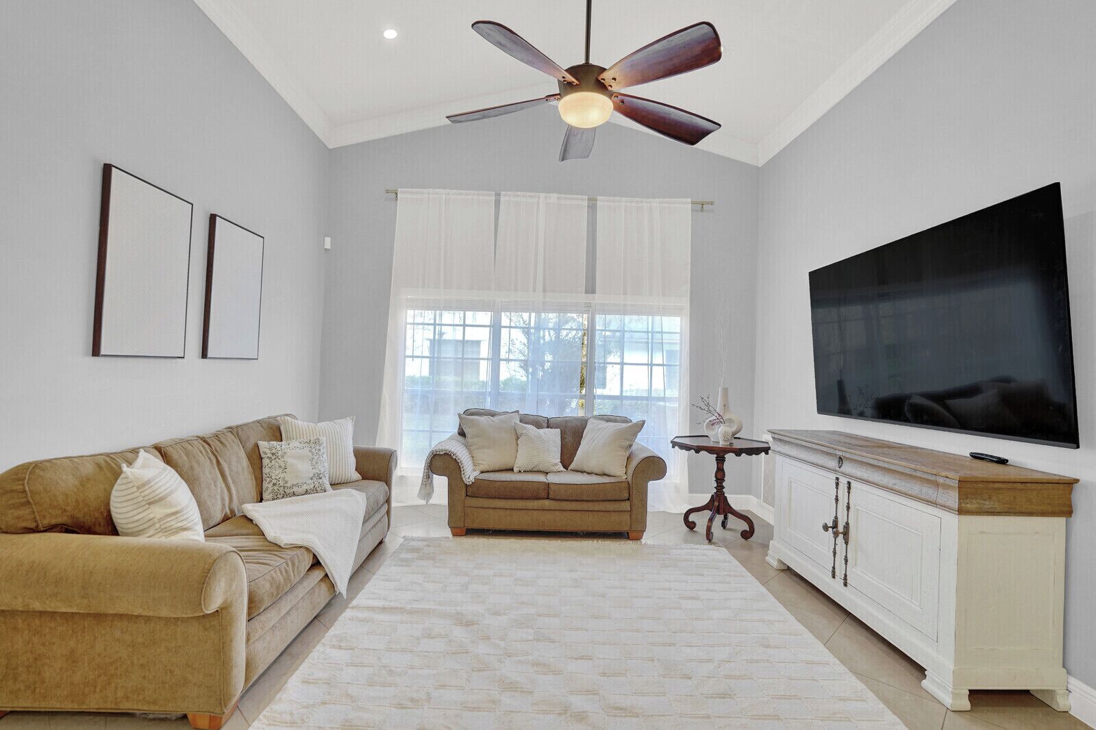 A living room with a beige sofa, a smaller sofa, a TV, and a ceiling fan.
