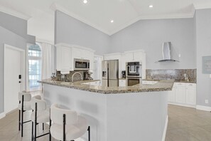Una cocina moderna con armarios blancos, encimeras de granito, electrodomésticos de acero inoxidable y una isla central con taburetes de bar.