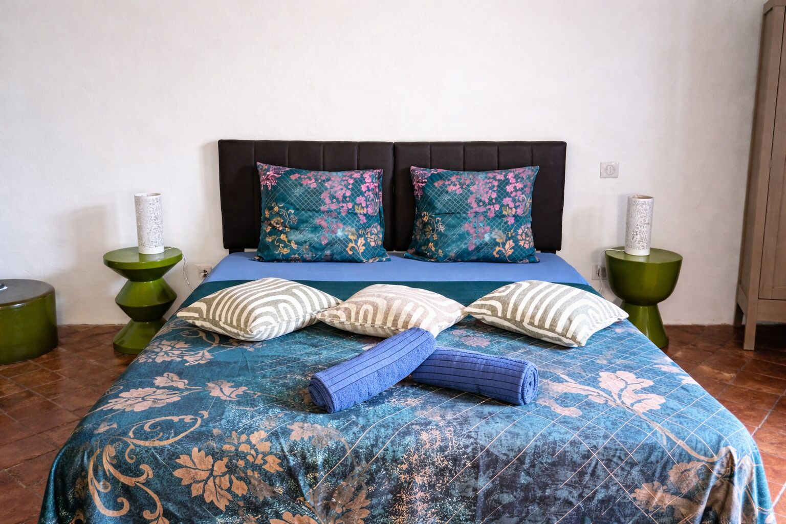 A bed with floral-patterned bedding, two pillows, and a rolled towel.