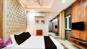 A modern hotel room with a tufted headboard, a flat-screen TV, a wooden cabinet, and a ceiling fan. - Super Deluxe Room Hotel Rockland (Kota)