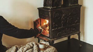 Iemand regelt een houtkachel met ingewikkelde houtsnijwerken en een vlam.