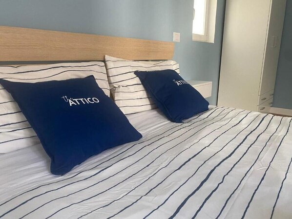 Un lit avec une literie à rayures et deux oreillers ornés du texte « The Attico ».