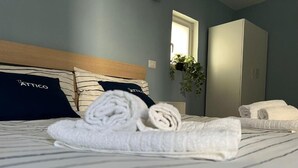 A neatly made bed with rolled towels and striped pillows, a window with a view of greenery, and a wardrobe in the background. - The Attic (Bari)