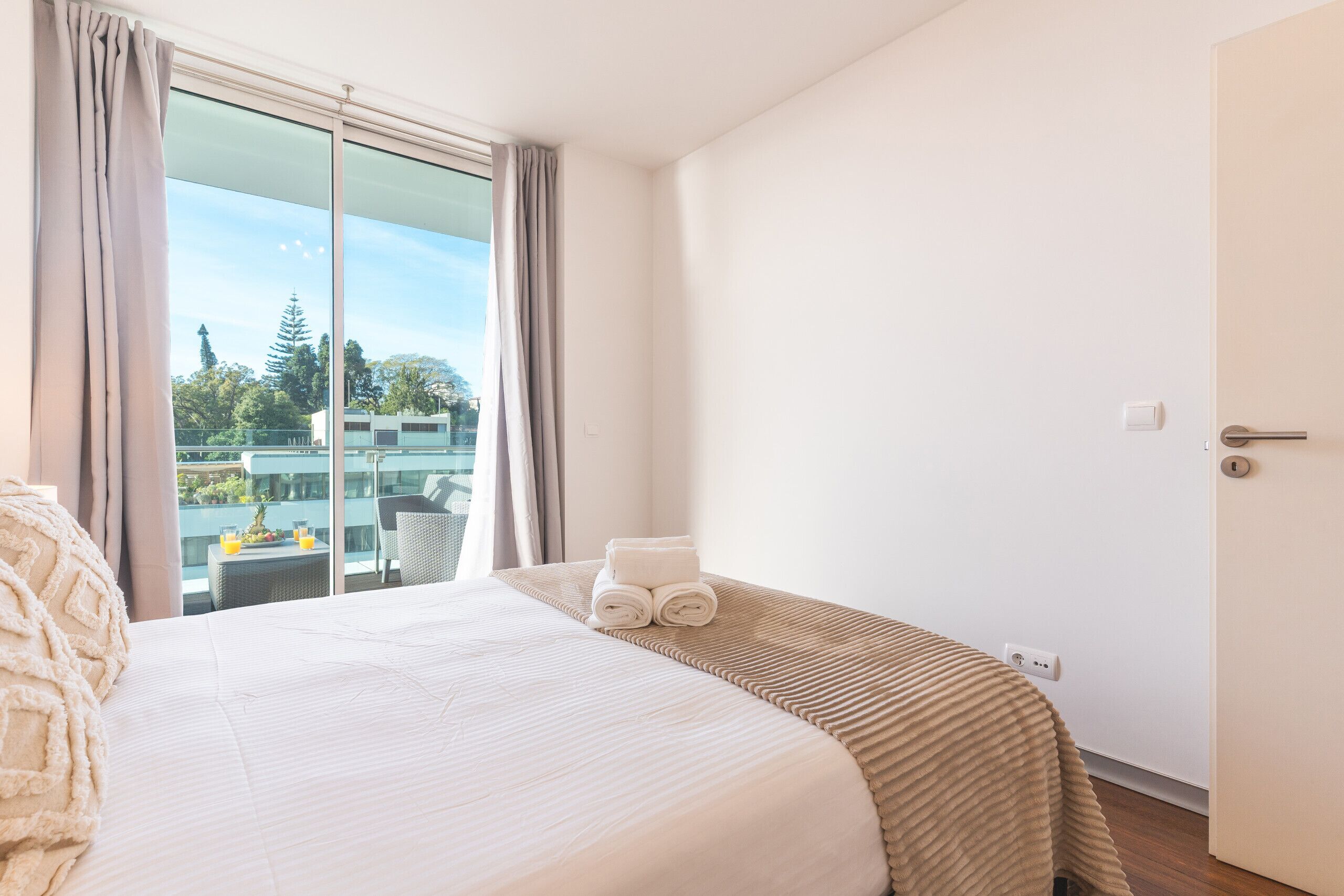 A hotel room with a large bed, a view of the outdoors, and a door to the right.